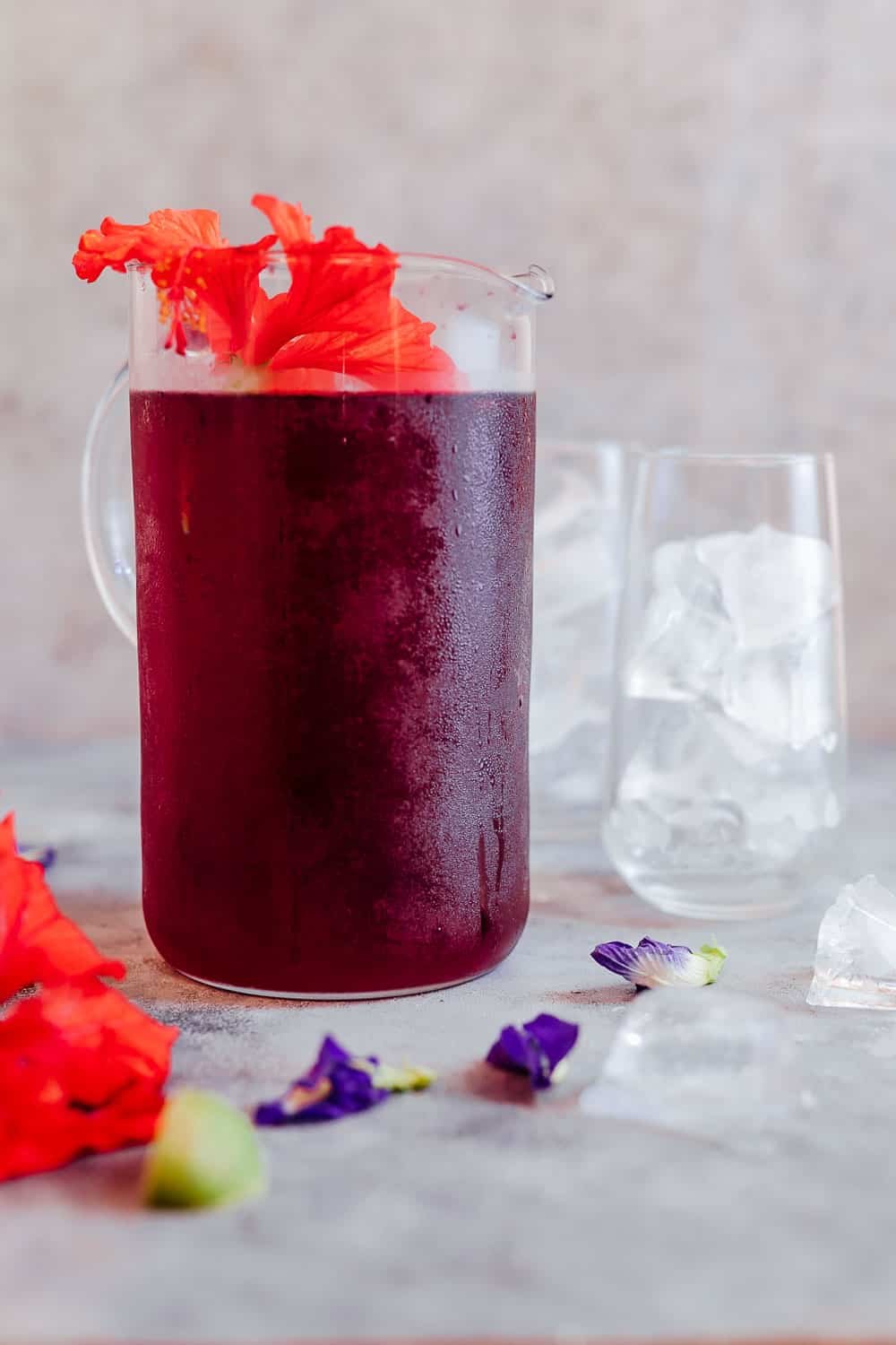 Chá de hibisco gelado servido em uma jarra grande com flores frescas de hibuscus