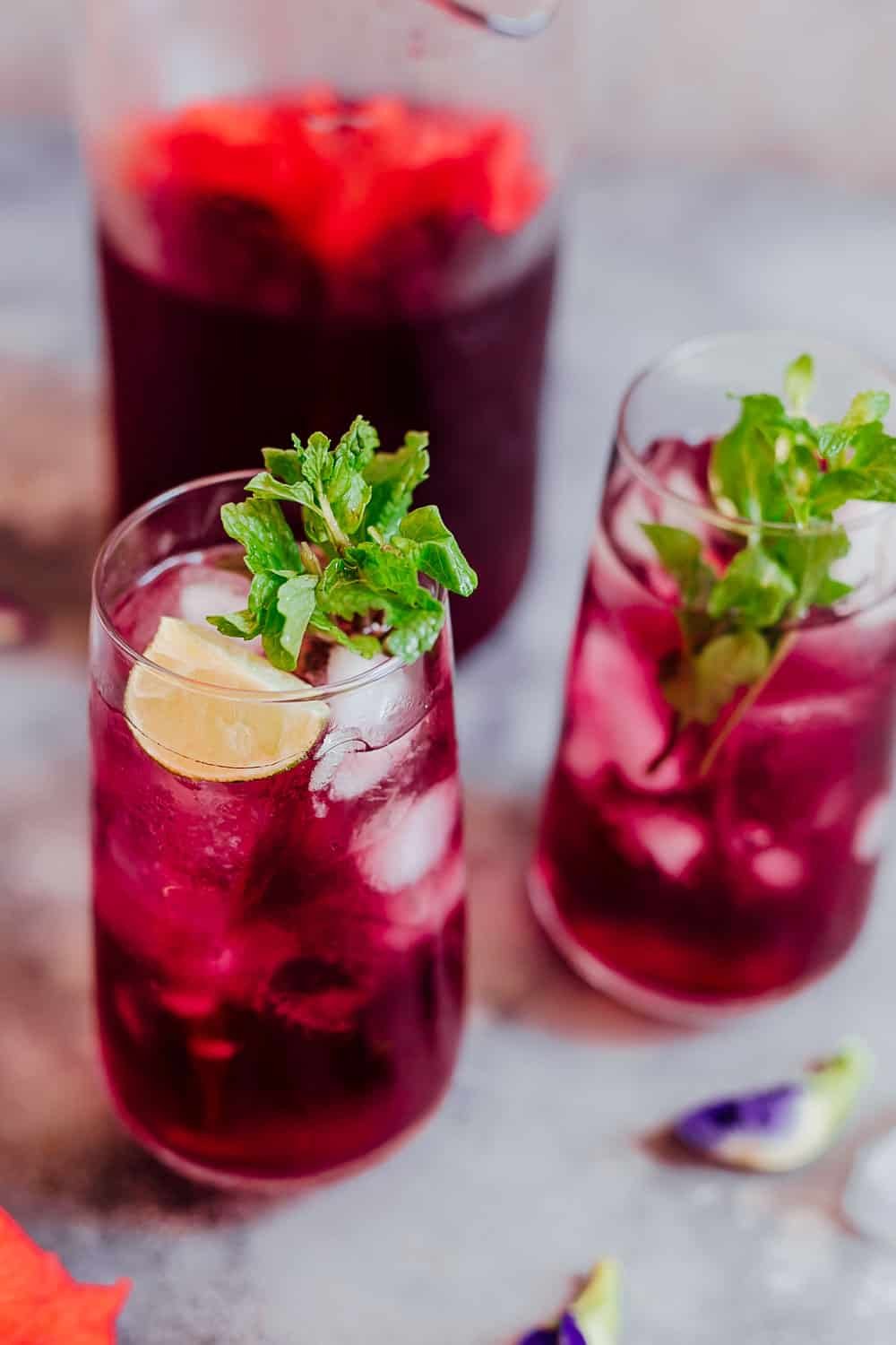 Close up de um copo de chá de hibisco com cubos de gelo, hortelã e limão
