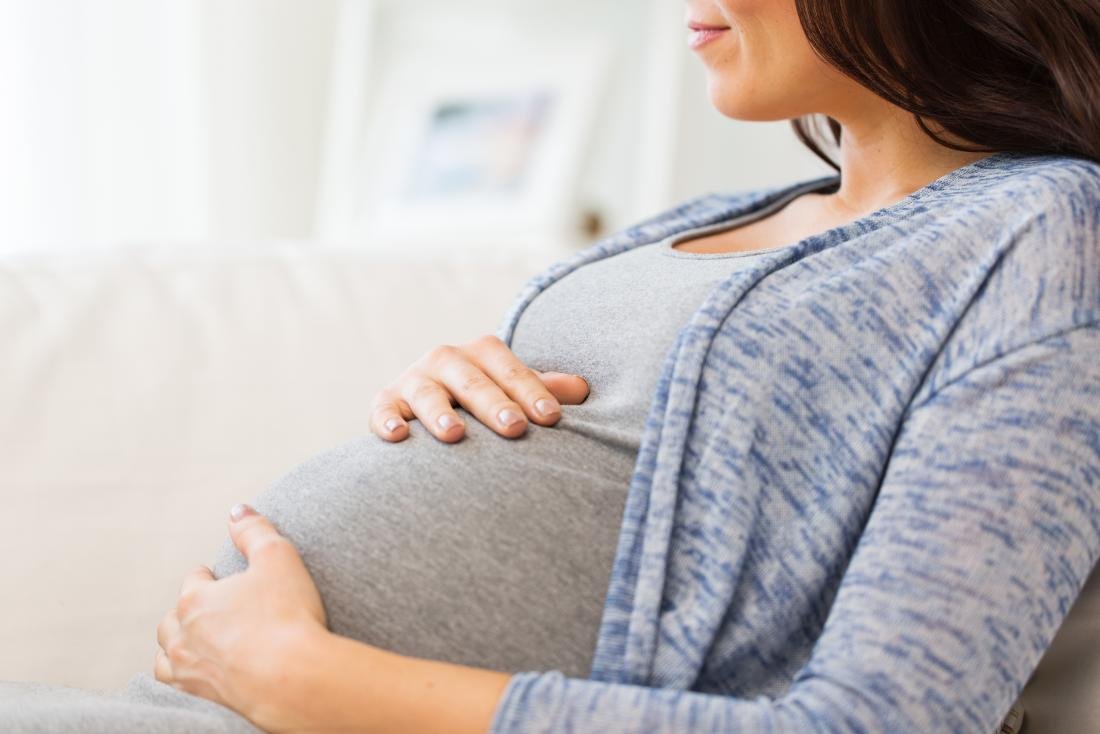 Mulher gravida que senta-se para baixo e que guarda sua colisão.